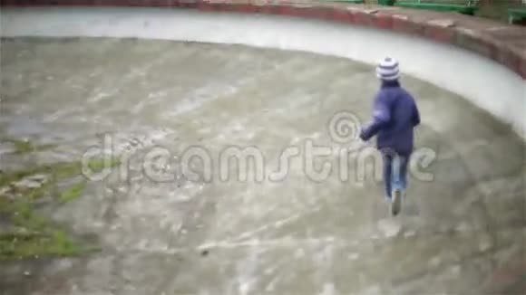 一个小男孩在一个空荡荡的大喷泉里奔跑慢动作视频的预览图