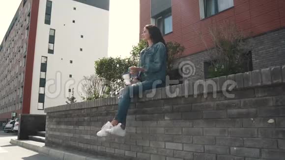 女孩在户外喝咖啡坐在栏杆上视频的预览图