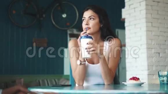 一个穿着休闲服的漂亮女孩从她的手机上发送信息年轻女孩在咖啡馆喝咖啡视频的预览图