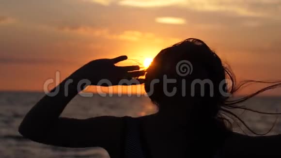 年轻快乐女人的剪影在令人惊叹的日落时分在海滩上慢动作地用耳机听音乐很有趣视频的预览图