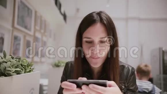年轻的女人用她的智能手机布鲁内特女孩微笑着手里拿着电话后台的人视频的预览图