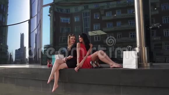 带着购物套餐的漂亮女孩正坐在一栋漂亮的蓝色玻璃建筑附近休息金发美女视频的预览图