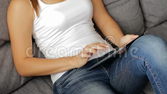 带电片的女人有平板电脑的女人坐在沙发上女士使用带有触摸屏的平板设备关闭视频的预览图