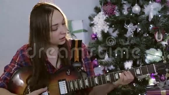 那个十几岁的女孩弹吉他在圣诞树附近唱着一首悲伤的歌视频的预览图