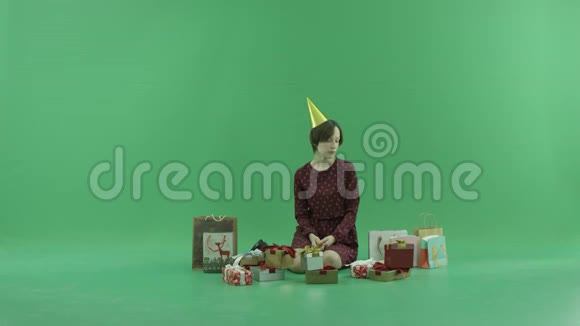 一个年轻的女人坐在绿色的屏幕上打开她周围的空礼品盒视频的预览图
