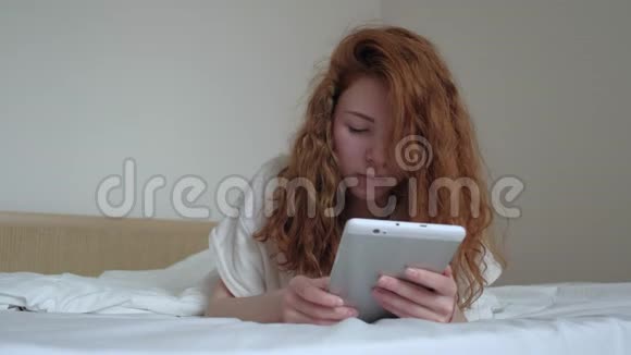 漂亮的红发女孩卧室里有一台数码平板电脑视频的预览图