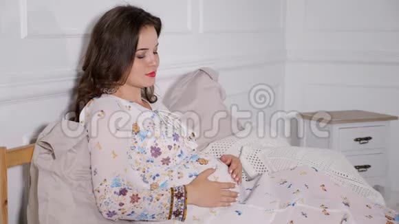 美丽的孕妇在床上拥抱视频的预览图