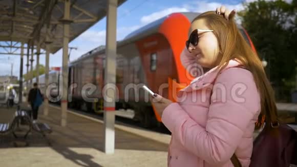 车站的年轻漂亮女人通过智能手机在线订购门票带眼镜长发粉色夹克视频的预览图