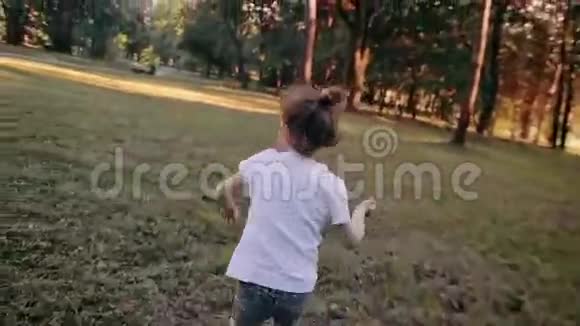 一个快乐的小女孩在一个阳光明媚的夏天从公园里的摄像机跑开后景慢影视频的预览图