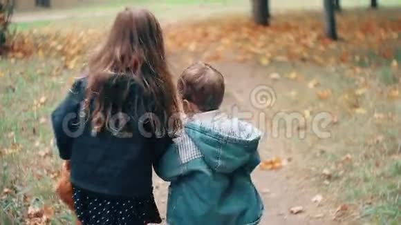 后景可爱的哥哥姐姐小男孩小女孩牵着手拿着玩具跑过秋天的小巷视频的预览图