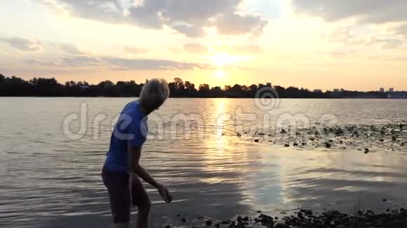 年轻人站在日落的河岸上他在斯隆磨石头视频的预览图