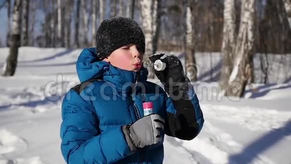 在一个阳光明媚的冬天男孩高兴地在公园里吹肥皂泡视频的预览图