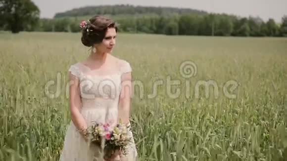 美丽的新娘站在麦田里穿着一件漂亮的白色连衣裙微笑着手里拿着一束花婚礼日视频的预览图