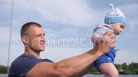 幸运的男孩子在湖边抱着儿子快乐的爸爸牵着第一个孩子在河边美丽的爸爸一起玩视频的预览图