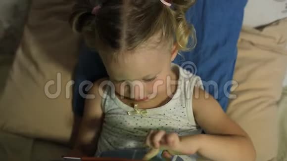 一个小女孩躺在床上的枕头上在平板电脑上玩游戏视频的预览图