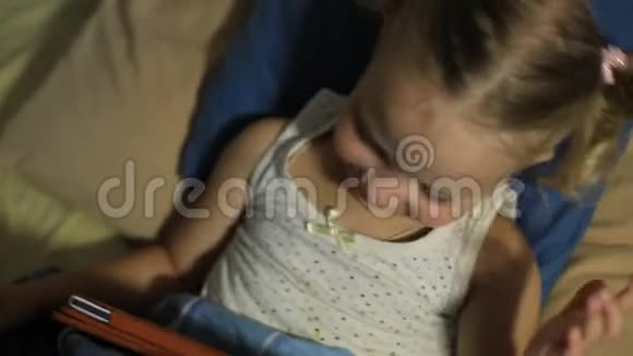 一个小女孩躺在床上的枕头上在平板电脑上玩游戏视频的预览图