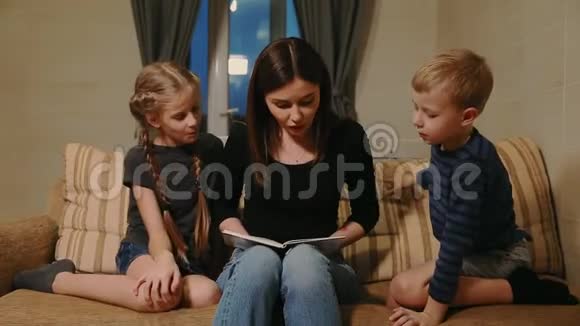 妈妈和他的女儿和小儿子一起坐在沙发上一边在沙发上看故事视频的预览图