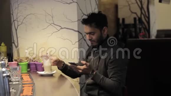 咖啡馆里年轻的黑人用手机喝咖啡视频的预览图