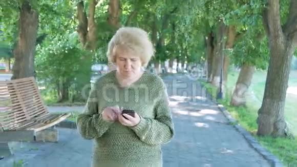 老年妇女使用智能手机步行公园车道在公园散步的高级女性视频的预览图