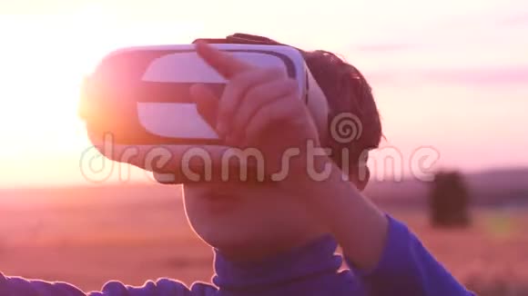 日落时分一个男孩戴着虚拟眼镜站在麦田里视频的预览图
