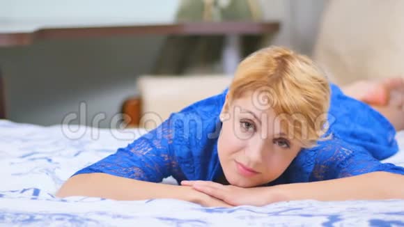 美丽的金发碧眼穿着蓝色连衣裙躺在床上视频的预览图
