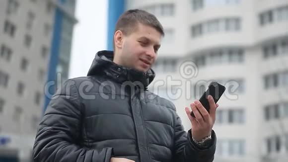 那个人在电话智能手机上说话冬天穿着冬季夹克的男人在户外摩天大楼智能手机上讲话视频的预览图