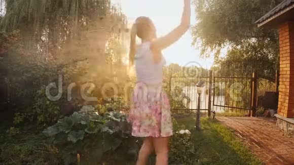 日落时花园喷水器溅水下快乐微笑女人的慢动作视频视频的预览图