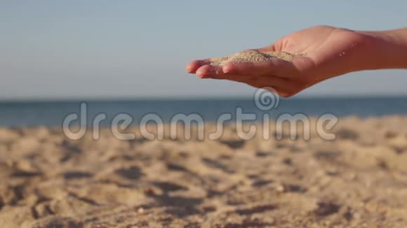 近距离观看从女人手中穿过的海沙在模糊的海洋上暑假的概念视频的预览图