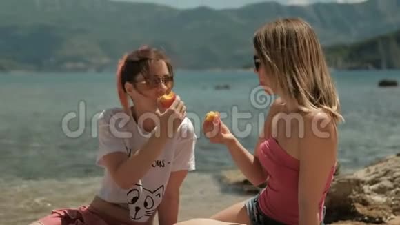 两个女人在阳光明媚的海滩上吃水果和交流视频的预览图