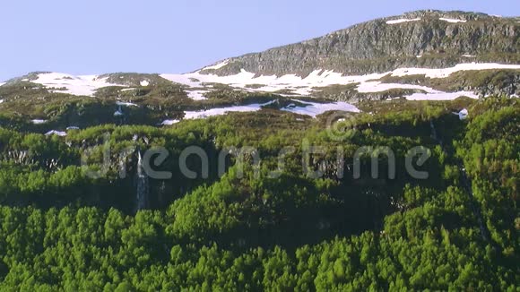 山峦的全景覆盖着绿色的树林夏天阳光明媚的一天山顶上有雪瀑布大自然视频的预览图