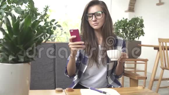 女人在咖啡馆里使用智能手机应用程序喝咖啡笑视频的预览图