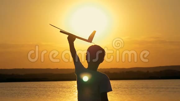 快乐的孩子在一个橙色的天空和湖泊的背景下在夏天日落玩玩具飞机视频的预览图