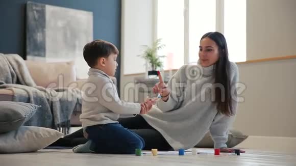母亲带着一个孩子在他的房子的白色内部被打开油漆罐坐在地板上蘸着你的水视频的预览图