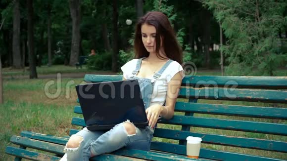 年轻可爱的黑发女人坐在长凳上手提电脑微笑着视频的预览图
