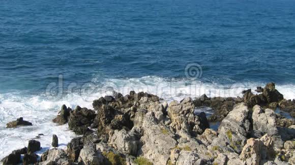 海滩上的岩石深蓝色的水面有温和的波浪视频的预览图