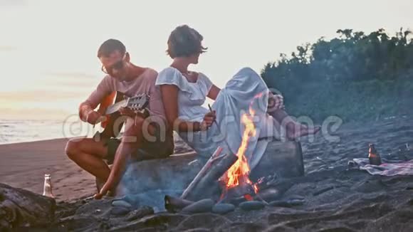 年轻夫妇在海滩上玩得很开心岛上的周末年轻夫妇在篝火旁弹吉他唱歌视频的预览图
