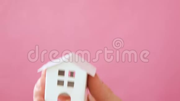 简单地设计女性手拿微型白色玩具屋孤立的粉红色粉彩五颜六色的时尚背景视频的预览图