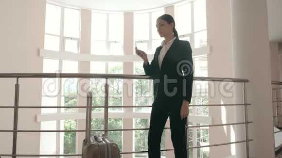 商务女性带着包在轮子上走路在酒店大堂里讲手机视频的预览图