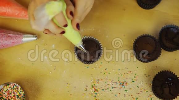 年轻女性手的俯视图用彩色奶油装饰巧克力纸杯蛋糕女人用糕点包视频的预览图