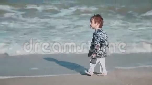 男孩年龄2岁外表漂亮在海边的沙滩上玩耍湿衣服和乐趣夏季一天视频的预览图