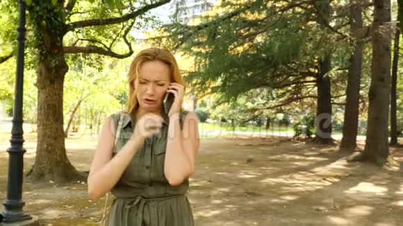 女人感到悲伤和哭泣在手机上和别人说话在夏天的公园里4k慢动作视频的预览图
