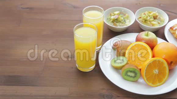 木桌上摆着两杯橙汁和一盘水果摄像机从左向右移动视频的预览图