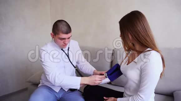 男医生在医院明亮的办公室里坐在沙发上测量女病人的血压视频的预览图