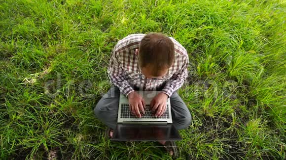 戴眼镜的年轻人坐在草地上打字视频的预览图