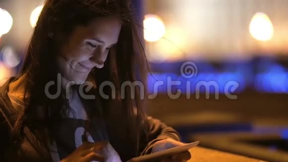 一个漂亮的年轻女人晚上用她的平板电脑她微笑风吹着她的头发模糊的背景缓慢的流动视频的预览图