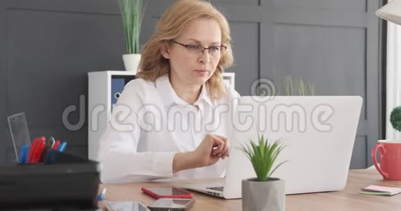 女商人在办公室使用笔记本电脑和手机视频的预览图