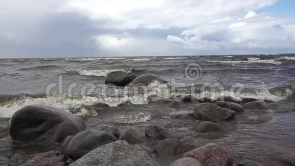 在多云的天空背景下大浪在芬兰湾海岸的石头上缓慢移动视频的预览图