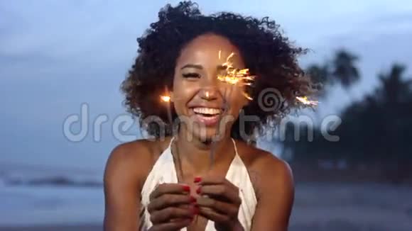 一个美丽的女人在沙滩上慢动作地拿着火花庆祝的夜晚视频的预览图