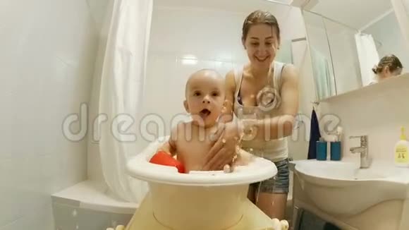 年轻漂亮的母亲在小塑料浴缸里缓慢地给婴儿洗澡视频的预览图