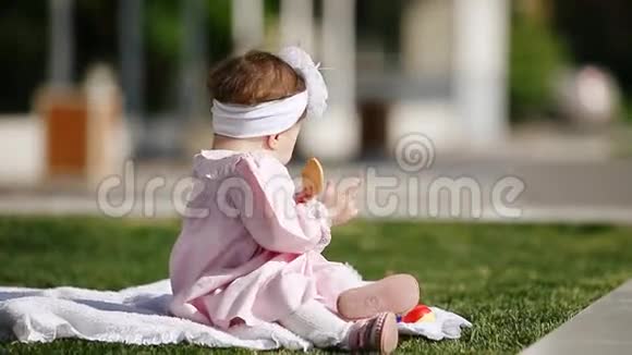 美丽的女婴坐在绿草上在公园里吃烤面包视频的预览图